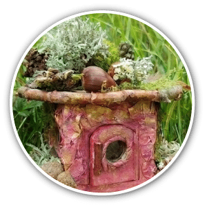 Icône circulaire présentant une petite maisonnette de fée miniature fabriquée en éléments naturels (écorce, mousse, brindilles) dans l'herbe.