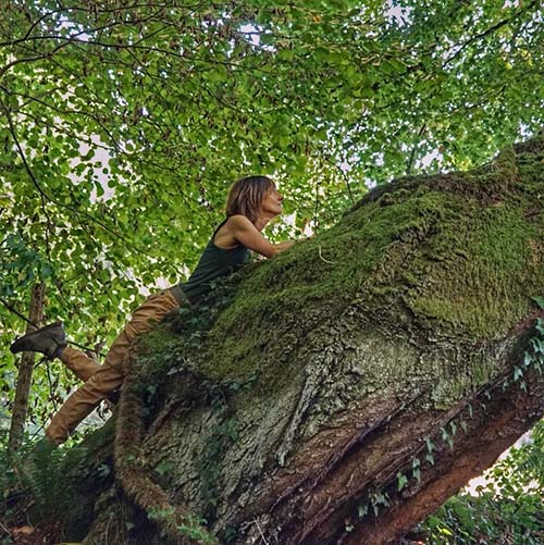 Portrait de Virginie, guide de sylvothérapie, enlacée contre un tronc d'arbre moussu en forêt pour illustrer la connexion nature - À fleur d'écorces.