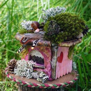 Vue de 3/4 du Refuge Framboise Dorée, création unique en carton et éléments de la nature glanés dans les forêts de la Montagne Noire et ailleurs. Façade en bâtonnets roses et dorés avec cœur en plaquage de bois peint en rouge.